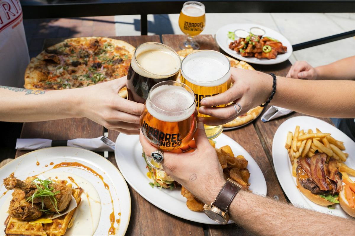 Mãos brindando com chope sobre mesa com pizza, batata frita e petiscos