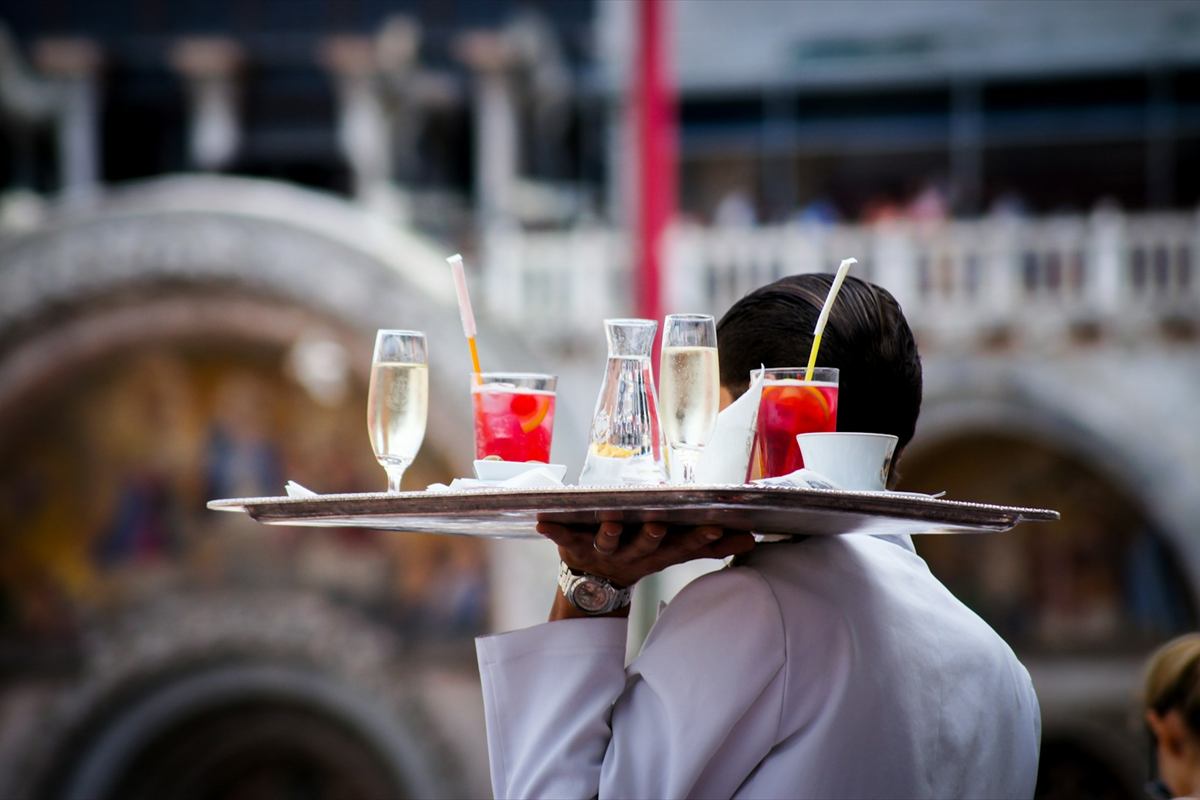 Garçom de costas carregando bandeja com espumante e drinques