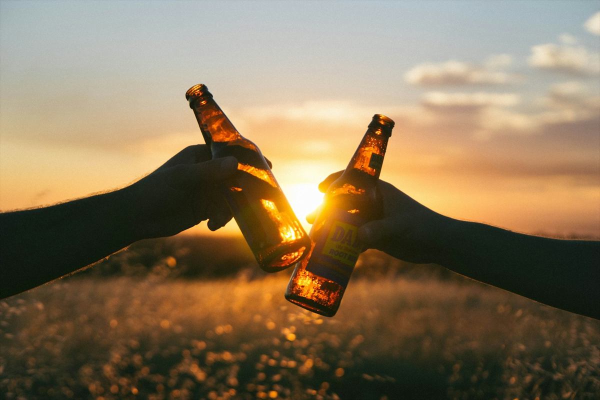 Duas mãos brindando com garrafas de cerveja no pôr do sol