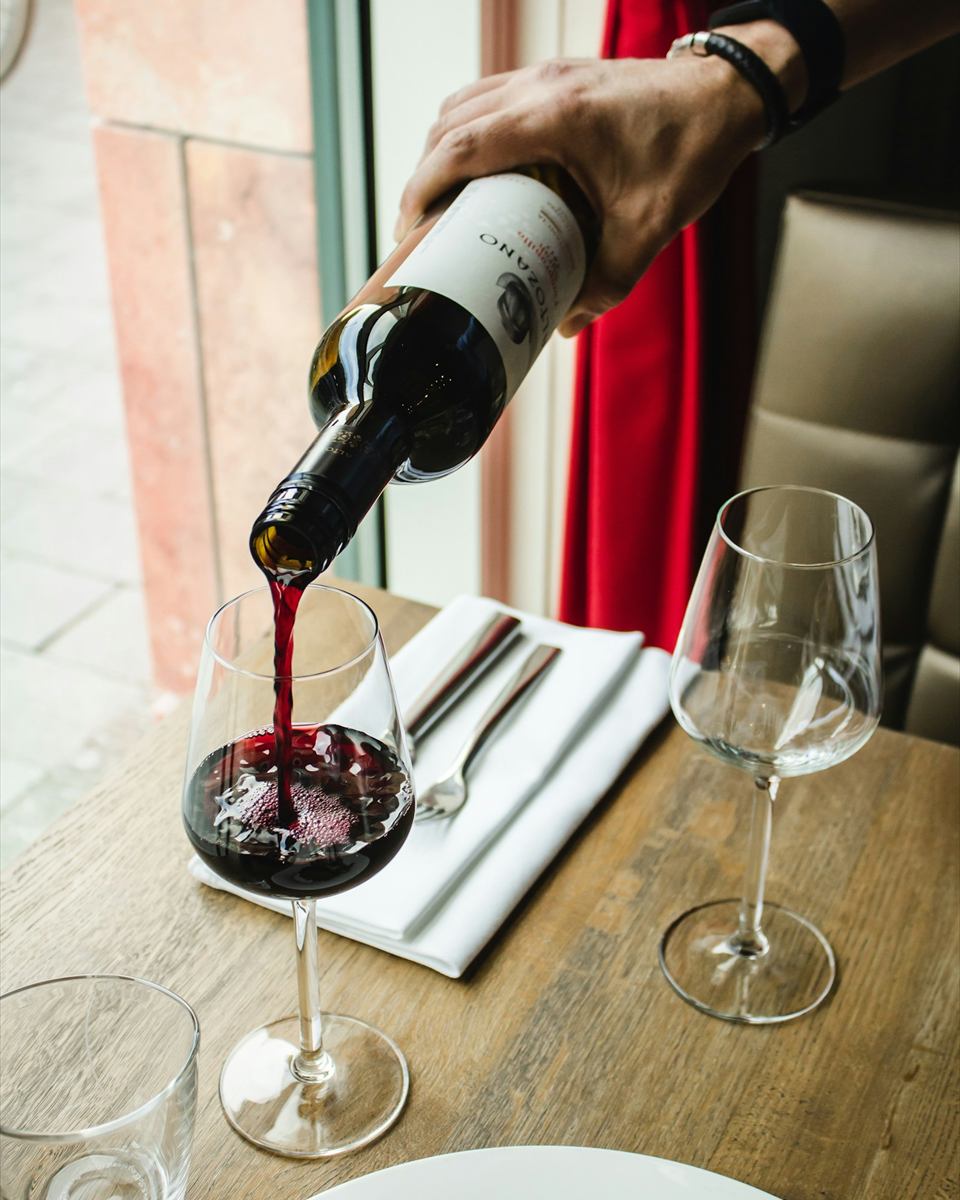 Mão servindo vinho tinto em taça sobre mesa posta